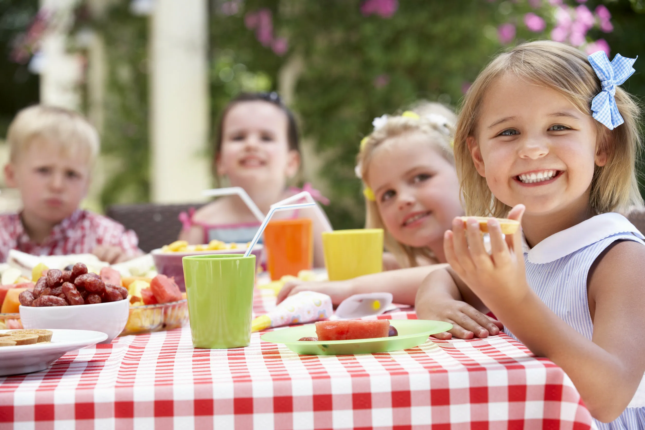 Auf dem Bild sind 4 Kinder, 2 Jungen und 2 Mädchen zu sehen, die an einem gedeckten Tisch sitzen und Kuchen essen und sich darüber freuen und lachen.